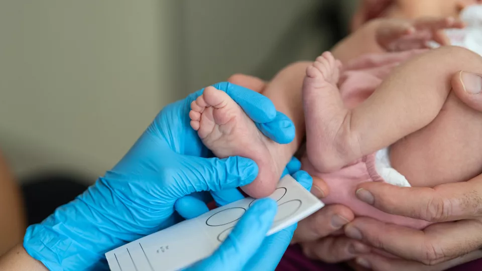 blue gloved hand measures infant foot