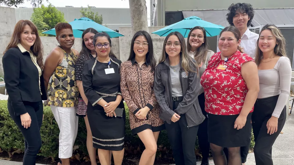 Young professionals smile as they stand in a single row and pose for outdoor picture