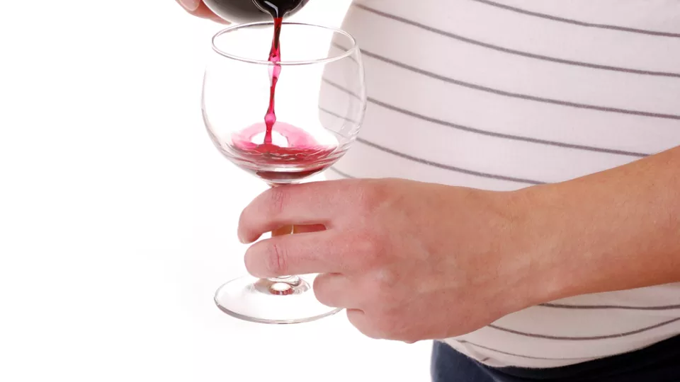 Pregnant woman with light skin tone pours glass of red wine