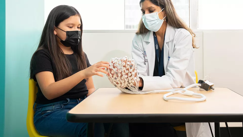 Shafali Spurling Jeste, MD demonstrates an electroencephalography cap with young girl