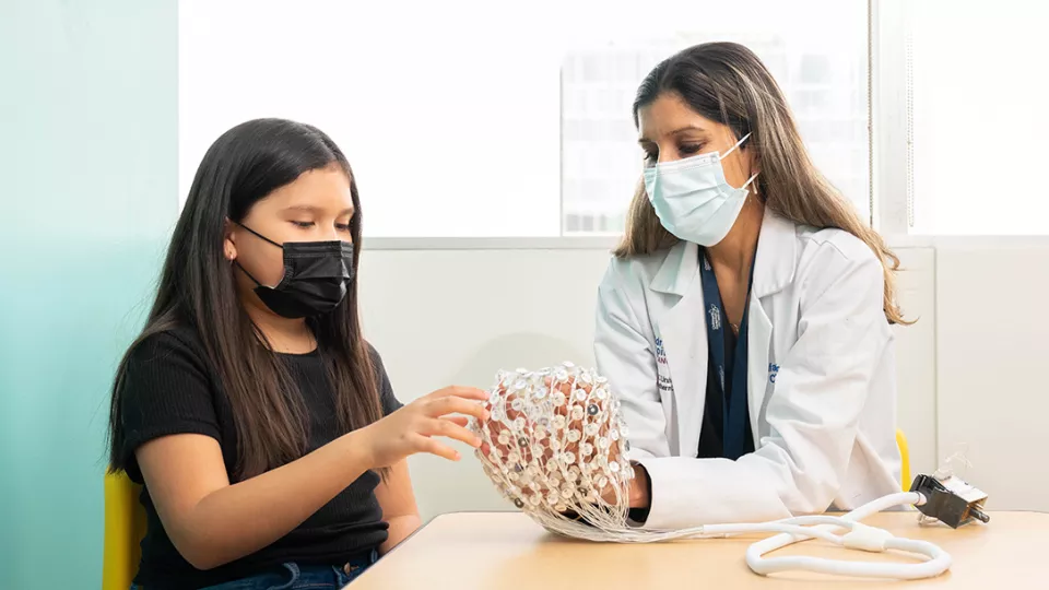 A girl and doctor both wearing medical procedure masks examine a model of a human brain.