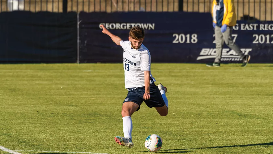 Young man with light skin tone wearing soccer uniform about to strike the ball as he takes a free kick