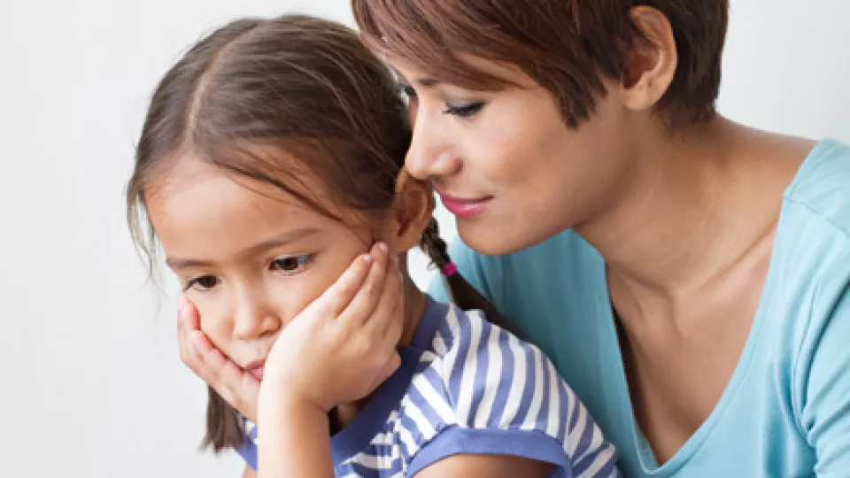 Young mother with medium skin tone and short brown hair comforts concerned-looking young daughter