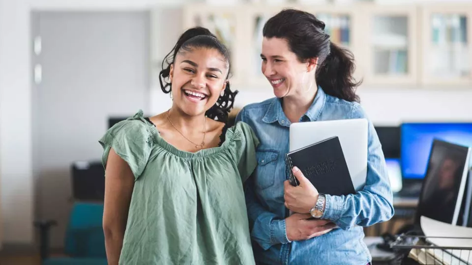 Smiling teenage girl stands next to a smiling woman holding a clipboard.