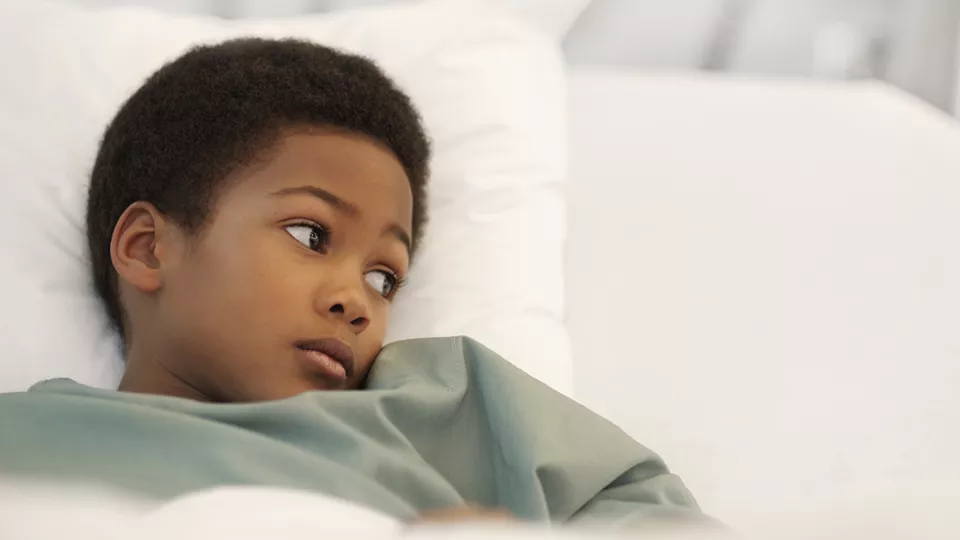 A young boy lays in a hospital bed, looking over to their left.