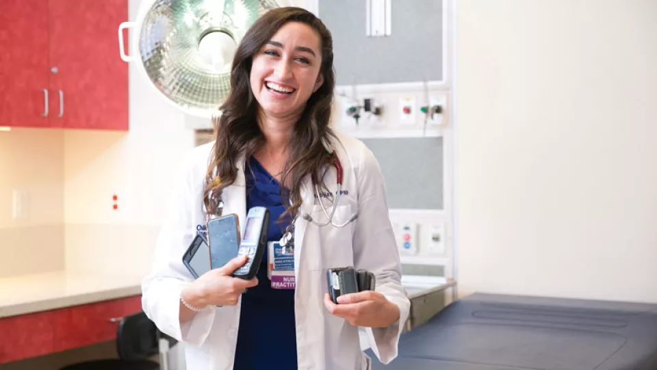 Smiling woman in a lab coat holds multiple cell phones.