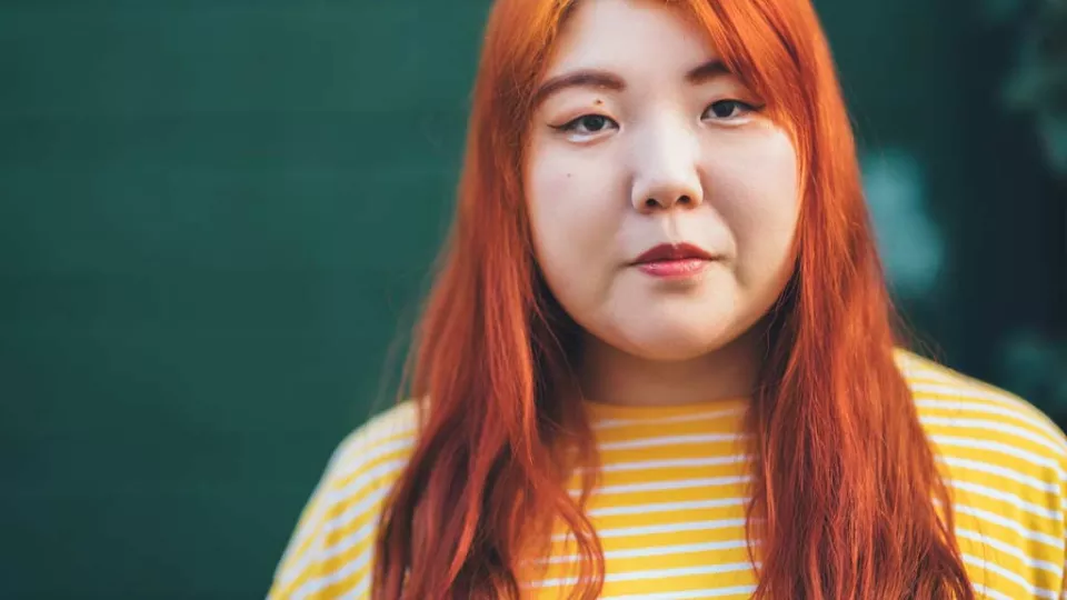 Portrait of a woman with red-orange hair wearing a yellow shirt.