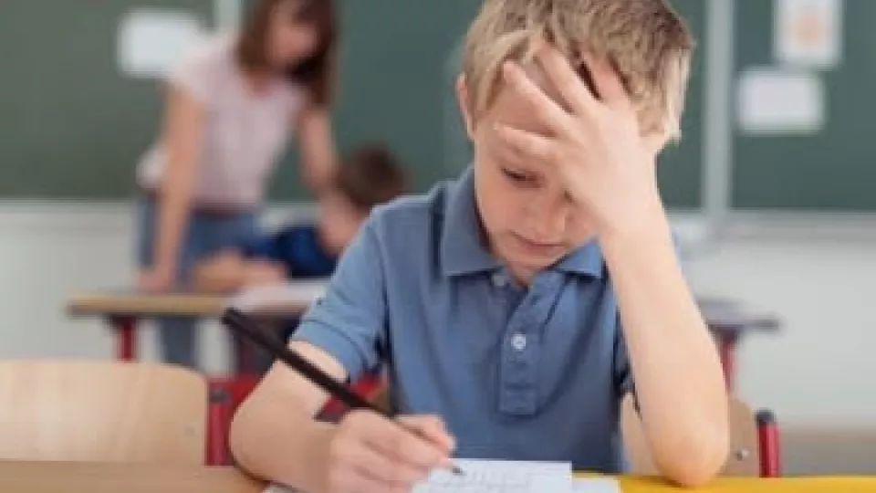 Young boy with light skin tone looks distressed as he works on a problem at school