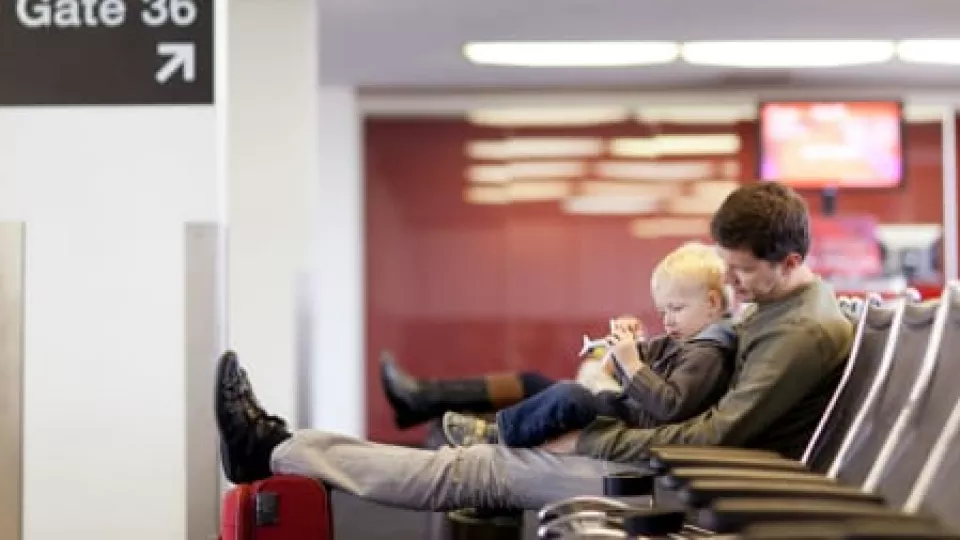 Father with light skin tone holds young son in his lap while waiting at the airport