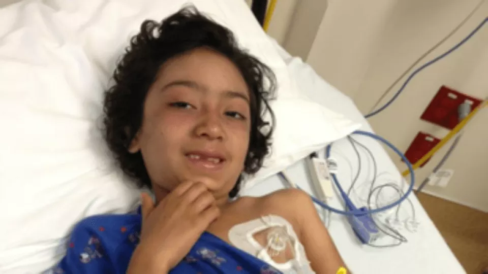 Girl with medium skin tone and dark hair rests on pillow with medical sensor attached to her chest