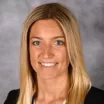 Headshot of a smiling woman with medium skin tone and long blonde hair wearing a dark jacket against a neutral indoor background