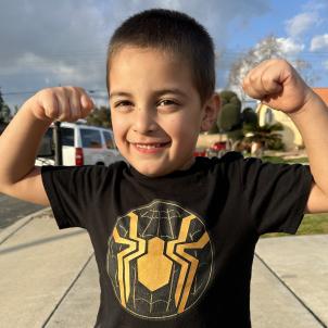 Young boy with medium skin tone and short dark hair smiles and flexes his biceps on a bright sunny day