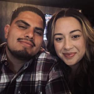 Young couple with medium skin tone and brown hair pose for an indoor selfie