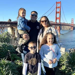Family of five smile for the camera as they pose for picture in front of the Golden Gate Bridge