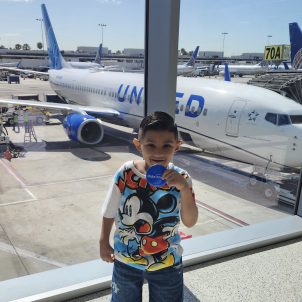 Nano stands in front of an airplane in the terminal of an airport. 