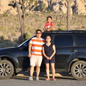 Family of three with light skin tone posing in front of SUV on road in the desert