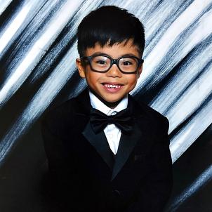 Young boy with light skin and dark wearing glasses and dressed in tuxedo