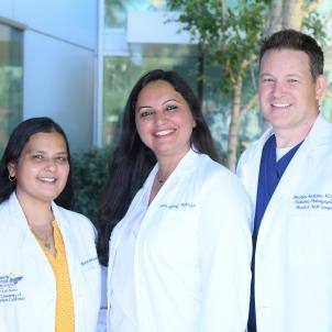 Two women and one man wearing white lab coats and smiling