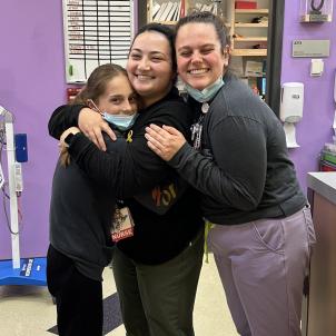 Young girl with light skin wearing mask hugging two young women with light skin