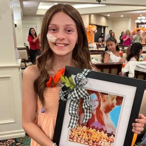 Young girl wearing orange dress smiling and holding framed photo