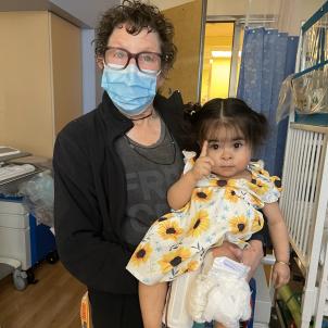 Woman wearing man holds baby in sunflower dress who is holding up her right forefinger