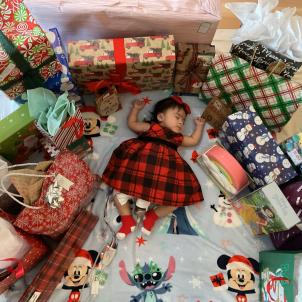 Baby in checkered dress lying on back asleep surrounded by wrapped gifts