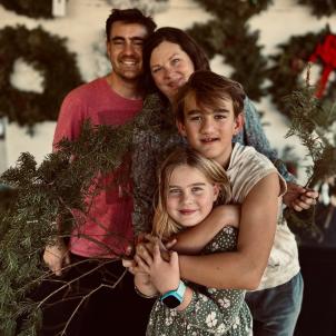 Two adults standing with two children in front of a wall of Christmas wreaths