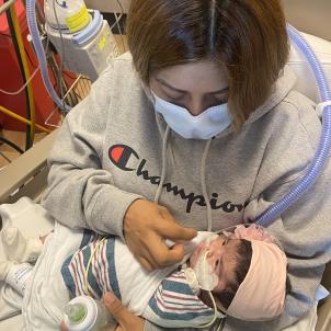 Woman wearing mask holding a bottle and feeding small baby