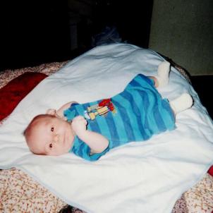 An infant Ryan lays on a bed and stares at the camera. 