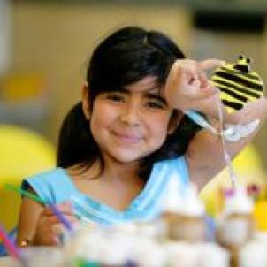 Smiling child doing a craft project, holding up a yellow and black bumble be that they painted.