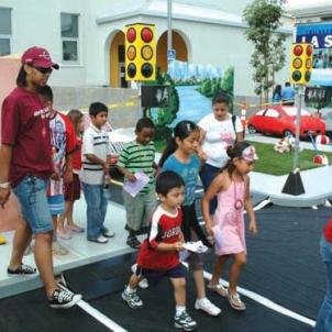 Children and adults walk across a set simulating a street light on a busy street