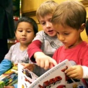 Young boy with light skin tone reads book as his friends look on