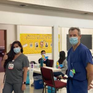 A medium skin toned woman in grey scrubs gives a thumbs up, and a light skin-toned man in blue scrubs smiles at the camera.