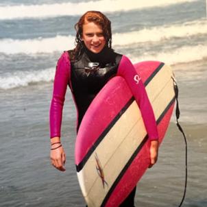 Sarah holing a surfboard by the ocean