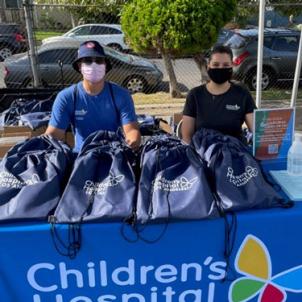 CHLA team members sitting at booth displaying bags with school supplies