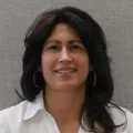 Headshot of a smiling woman with light skin tone and dark hair wearing a white blouse against a neutral background