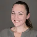 Headshot of a smiling woman with light skin tone and pulled back brown hair against an indoor neutral background