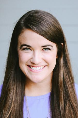 Headshot of a smiling woman with light skin tone and straight brown hair wearing a lavender top against a neutral indoor background