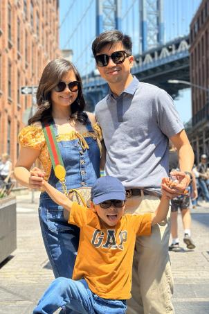 Woman and man with dark hair and light skin holding on to boy in orange shirt and blue cap