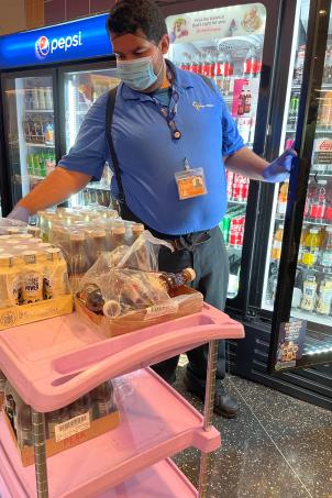 A medium skin-toned man in a polo shirt and surgical mask stocks drinks in a display cooler.