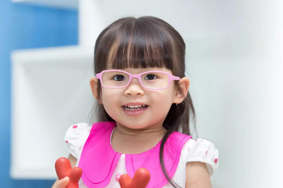 Smiling little girl with light skin tone, straight dark hair wearing pink eyeglasses