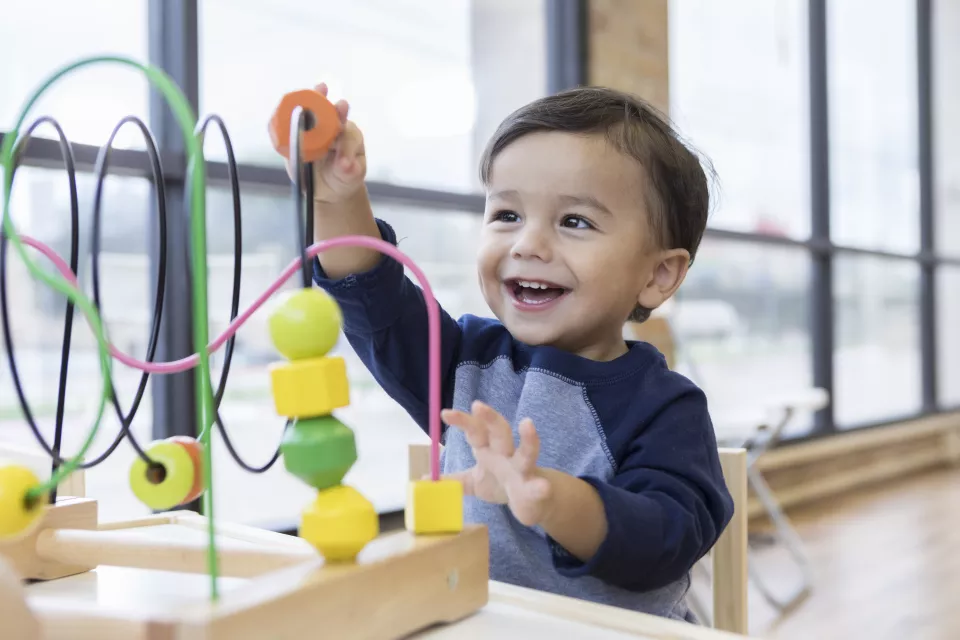 Smiling toddler with blue shirt playing with a colorful toy.