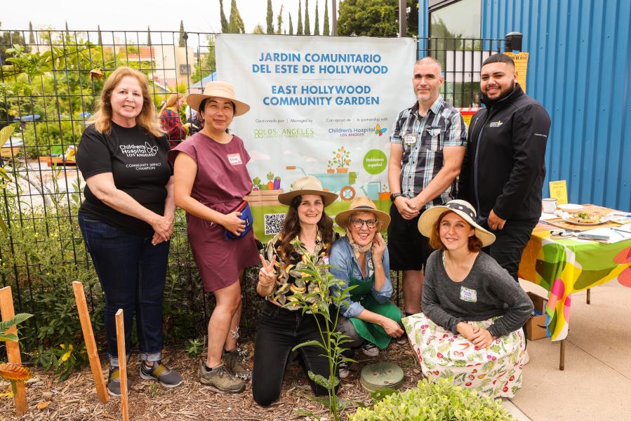 7 people smile, gathered around a banner that says East Hollywood Community Garden in English and Spanish.