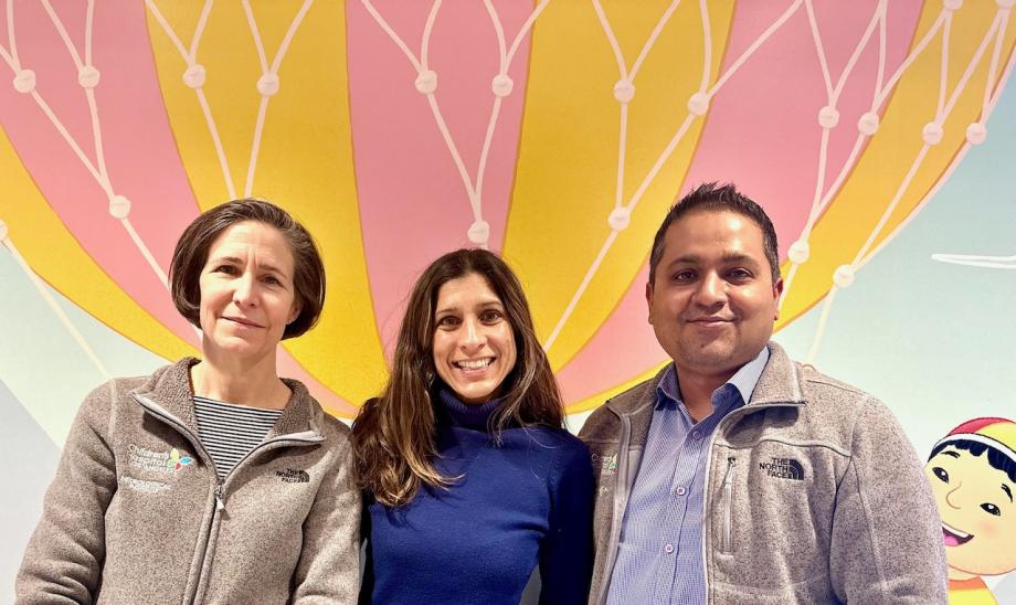 Drs. Rosser, Jeste and Vishwanath stand together, smiling, in front of a large drawing of a pink and yellow hot air balloon.