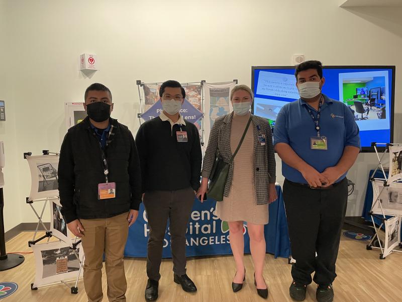 Four people in surgical masks pose together, in front of a table with a Children's Hospital Los Angeles banner