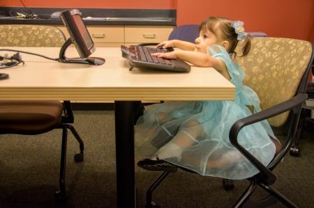 Angelique Garcia, a little girl sits at a desks and reaches out to touch the keyboard of a computer.